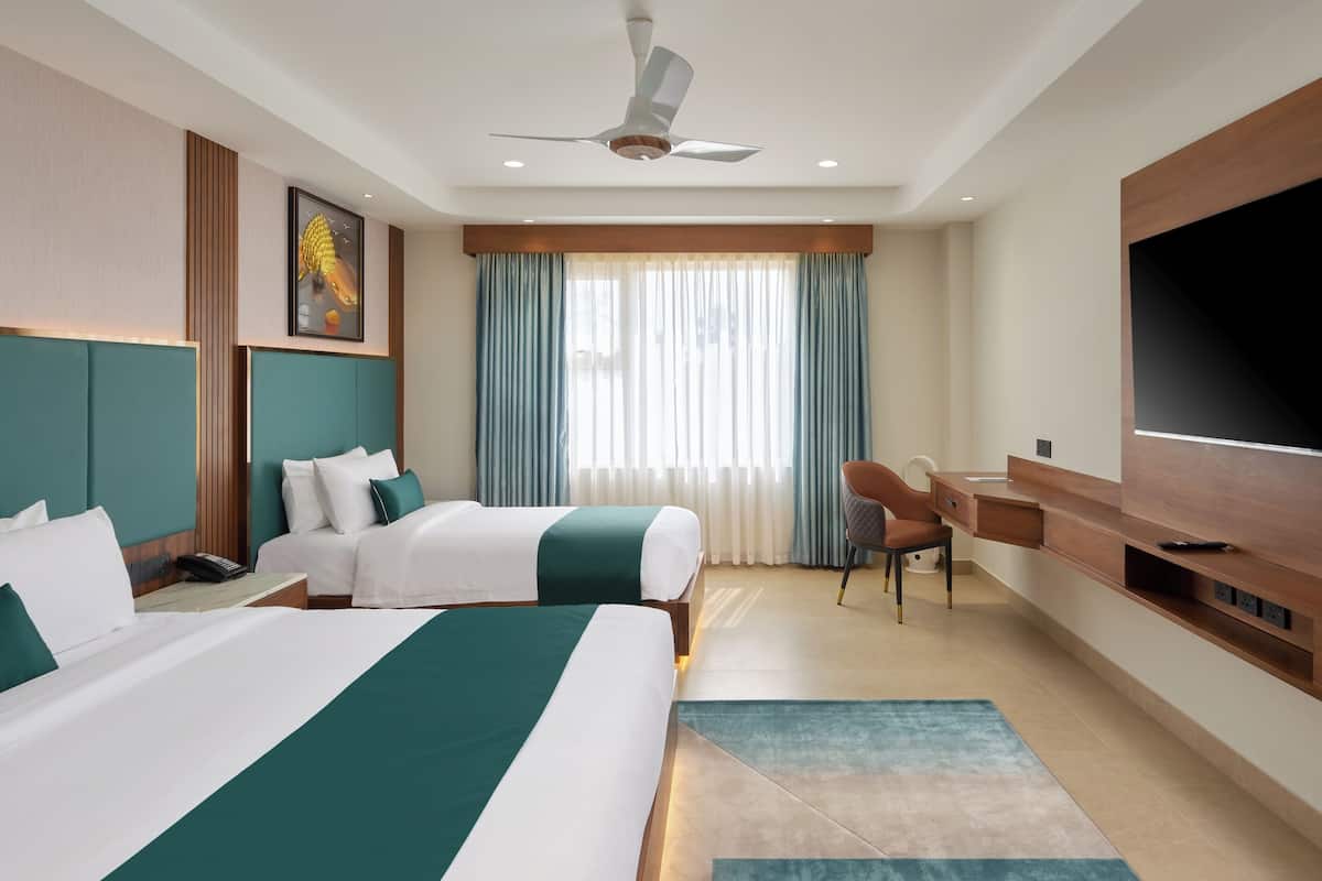 A hotel room with two beds, a desk, a chair, a TV, and a ceiling fan.