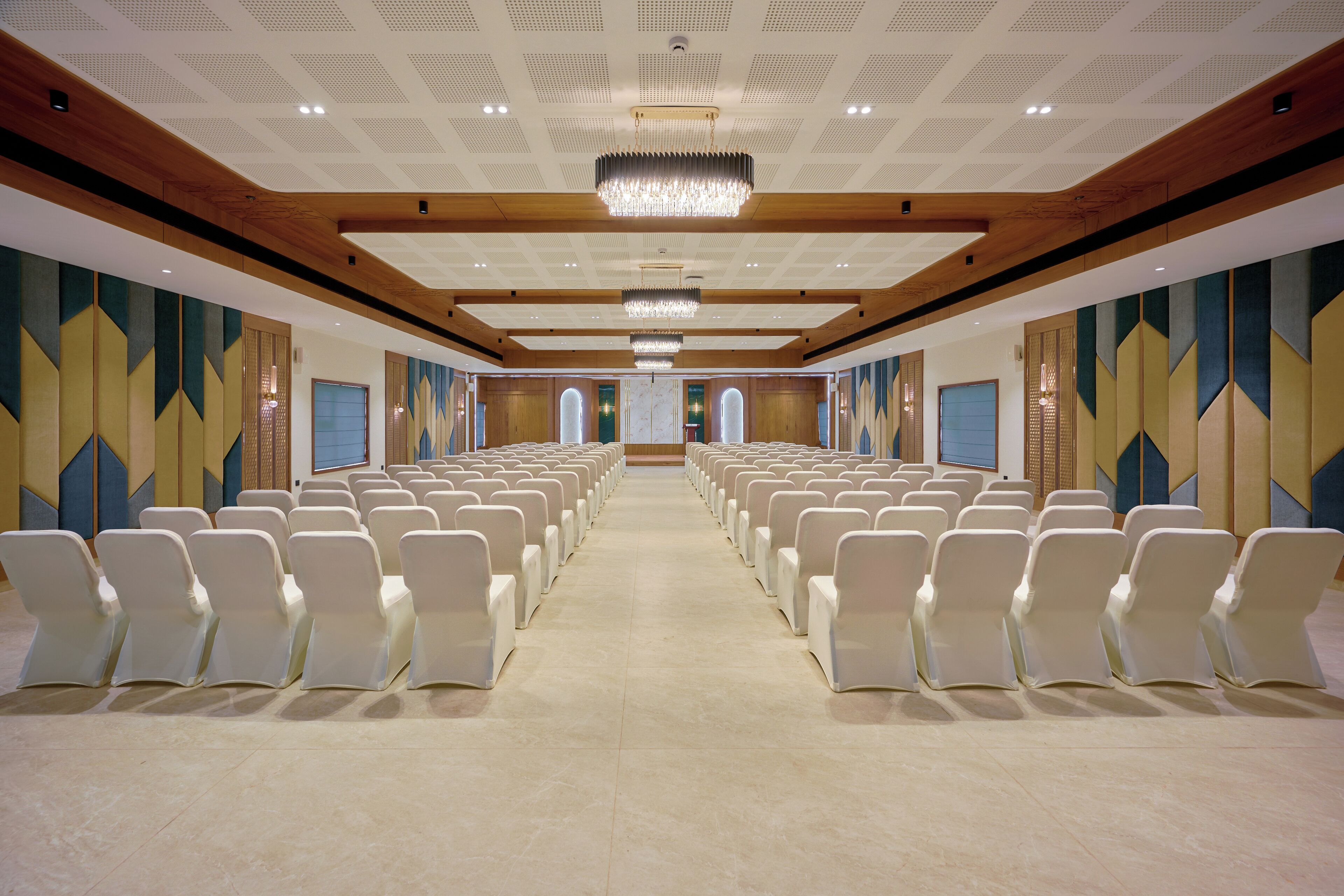 A conference room with rows of white chairs, a wooden ceiling, and geometric wall patterns.