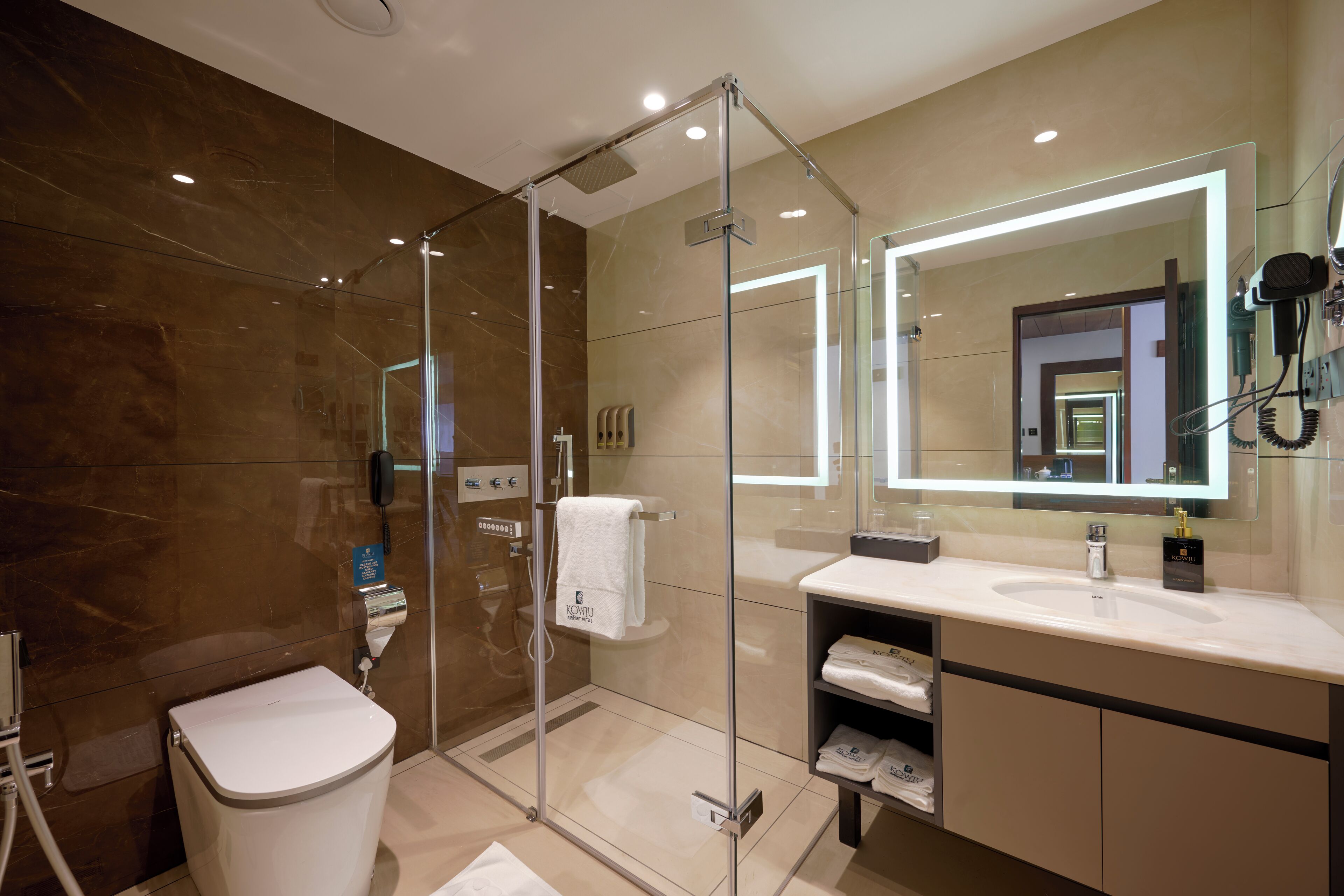 Une salle de bain moderne avec une douche à parois de verre, des toilettes blanches, un grand miroir et un meuble-lavabo.