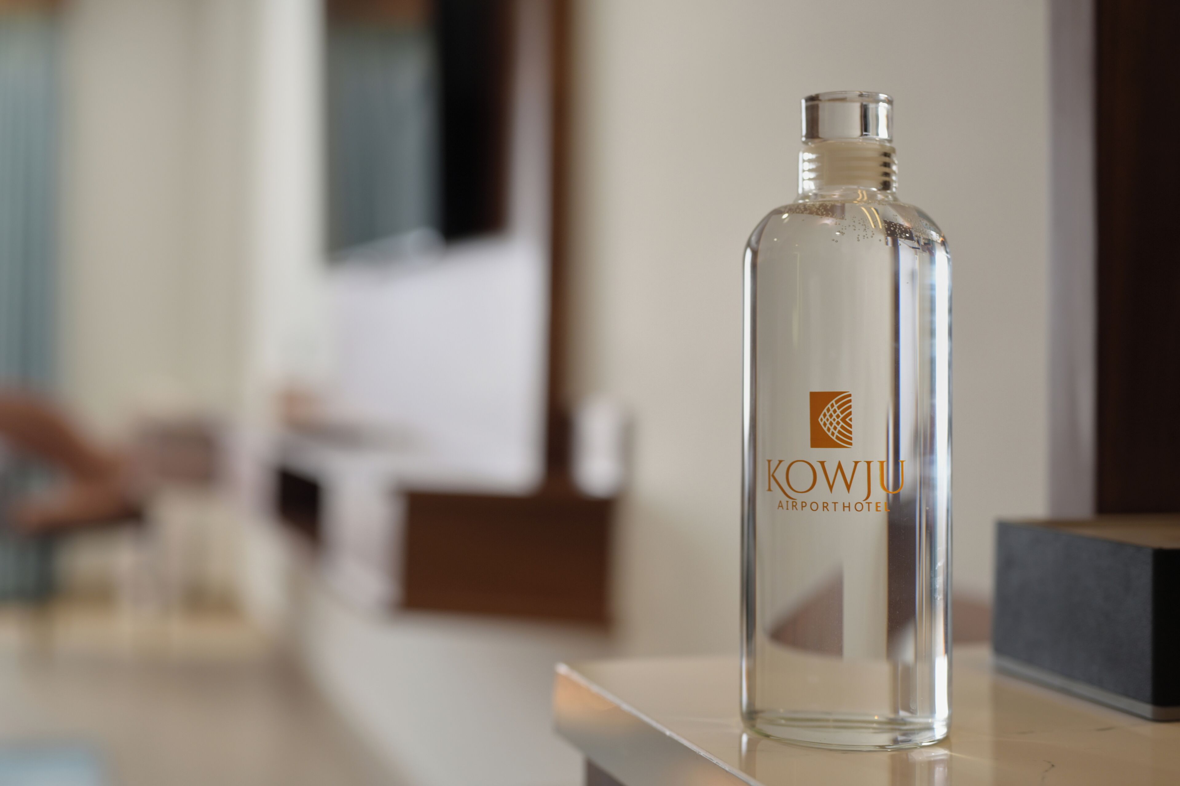 A clear bottle with the label "KOWJU Airport Hotel" on a reflective surface.