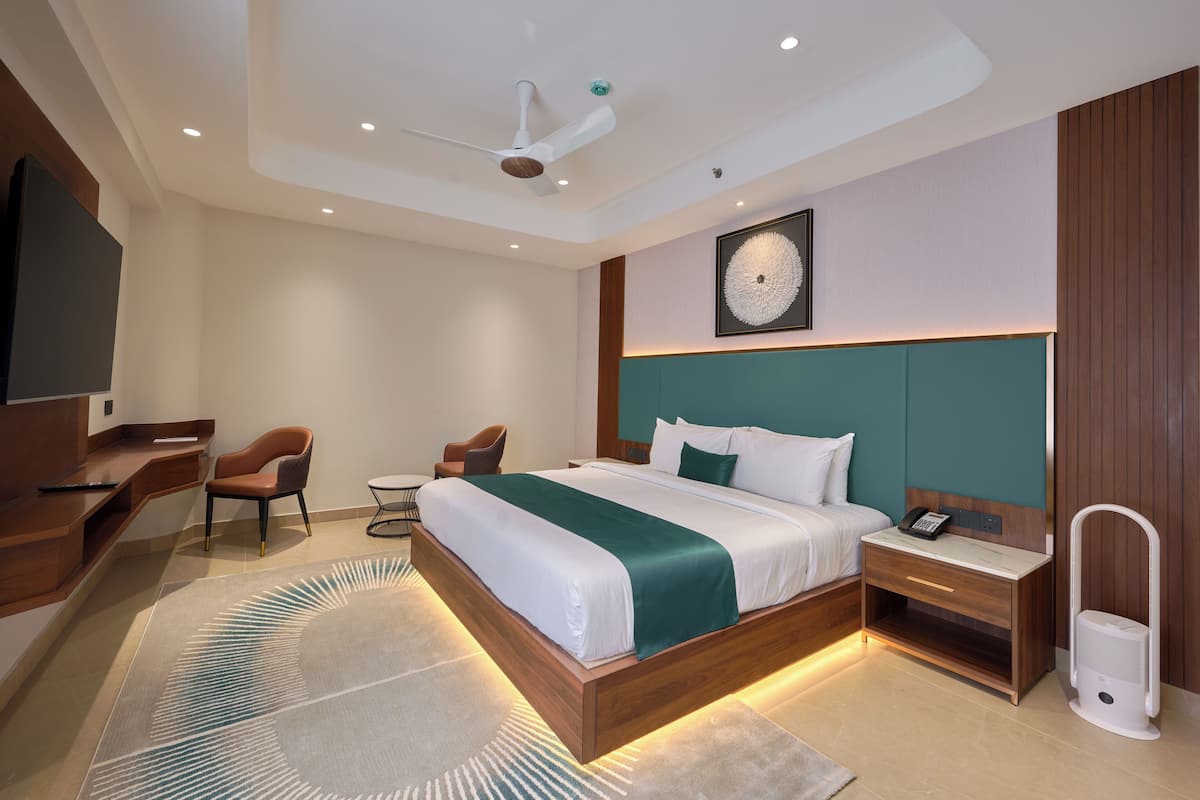 A modern hotel room with a large bed, a desk, a chair, and a bedside table with a phone.
