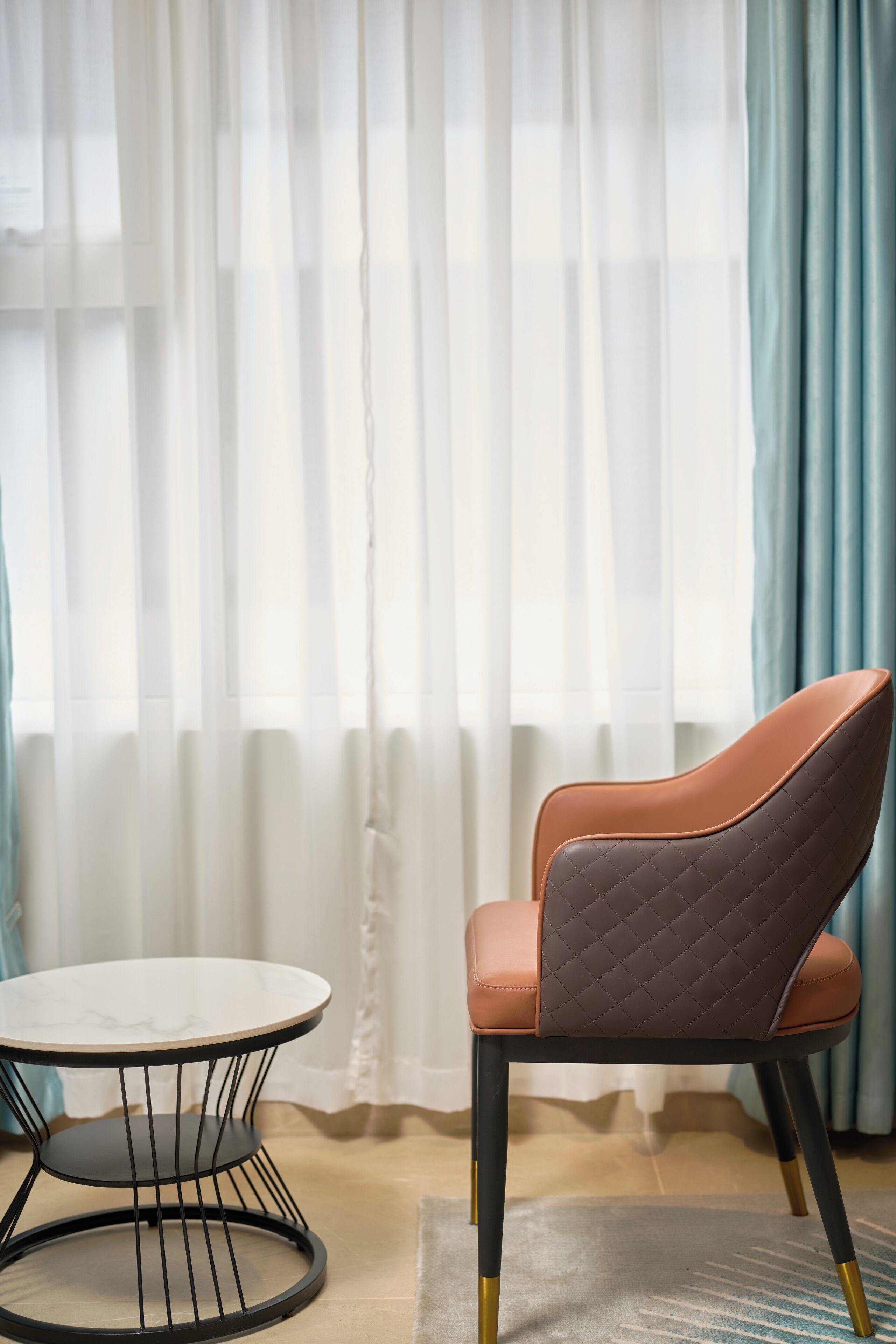 A chair with a quilted backrest and a round table with a wireframe base.