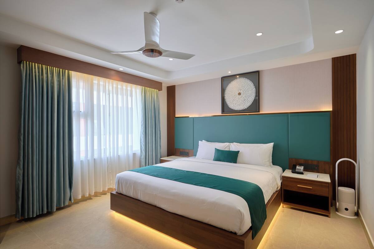 A modern hotel room with a large bed, a ceiling fan, a nightstand, and a framed artwork on the wall.