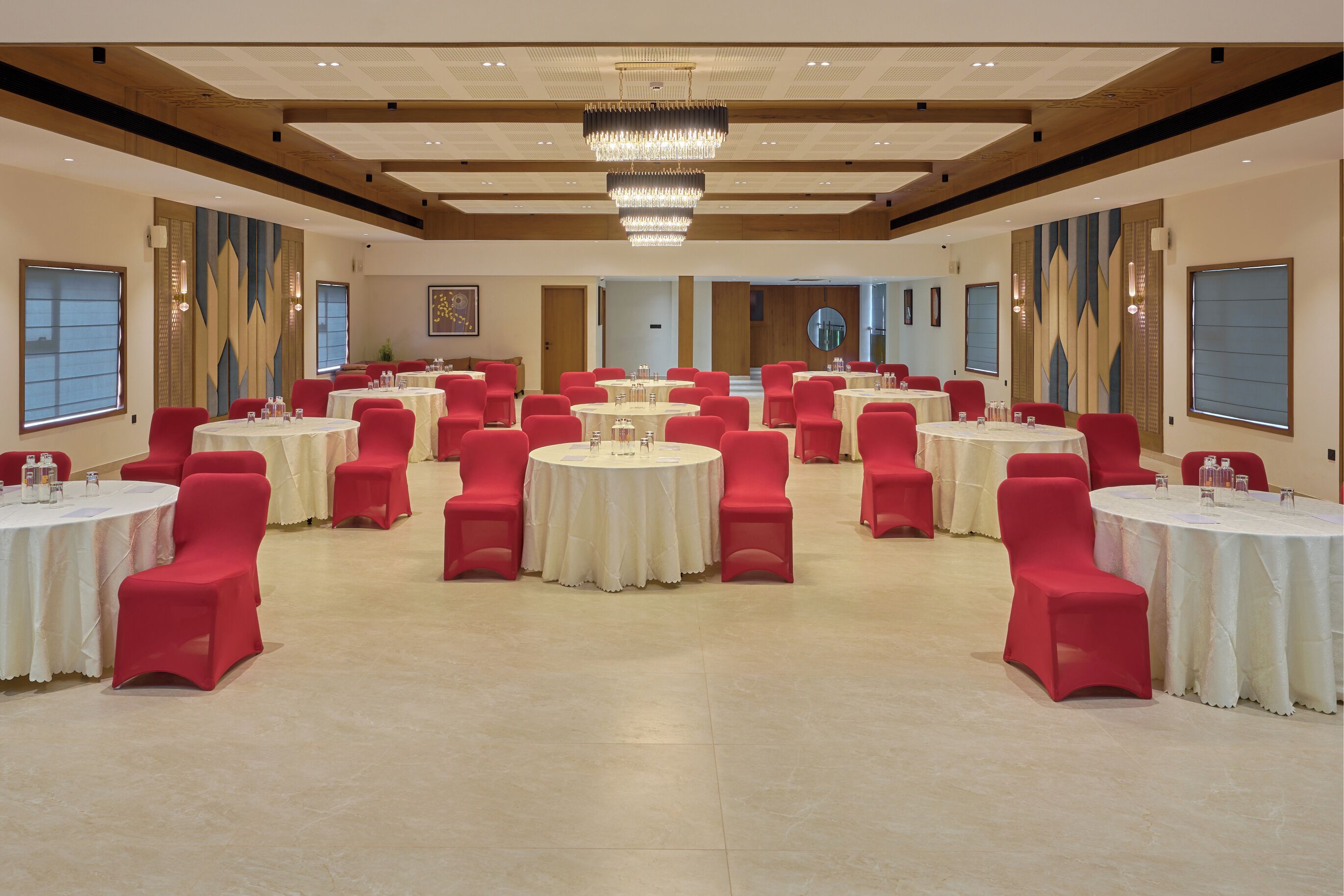 A spacious banquet hall with multiple round tables, red chairs, and a large chandelier.