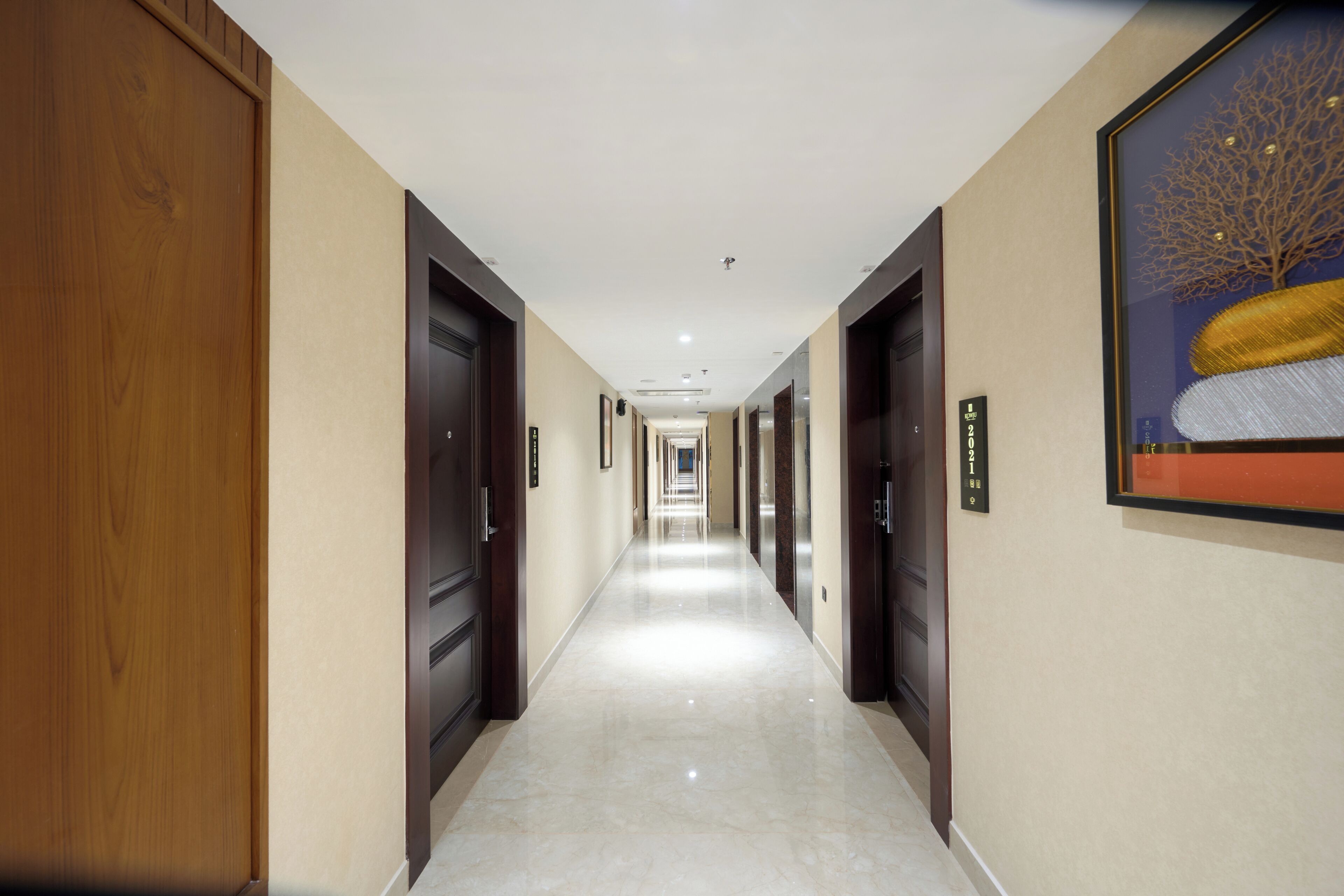 Un pasillo de hotel con puertas de madera, suelo de mármol y una obra de arte enmarcada en la pared.