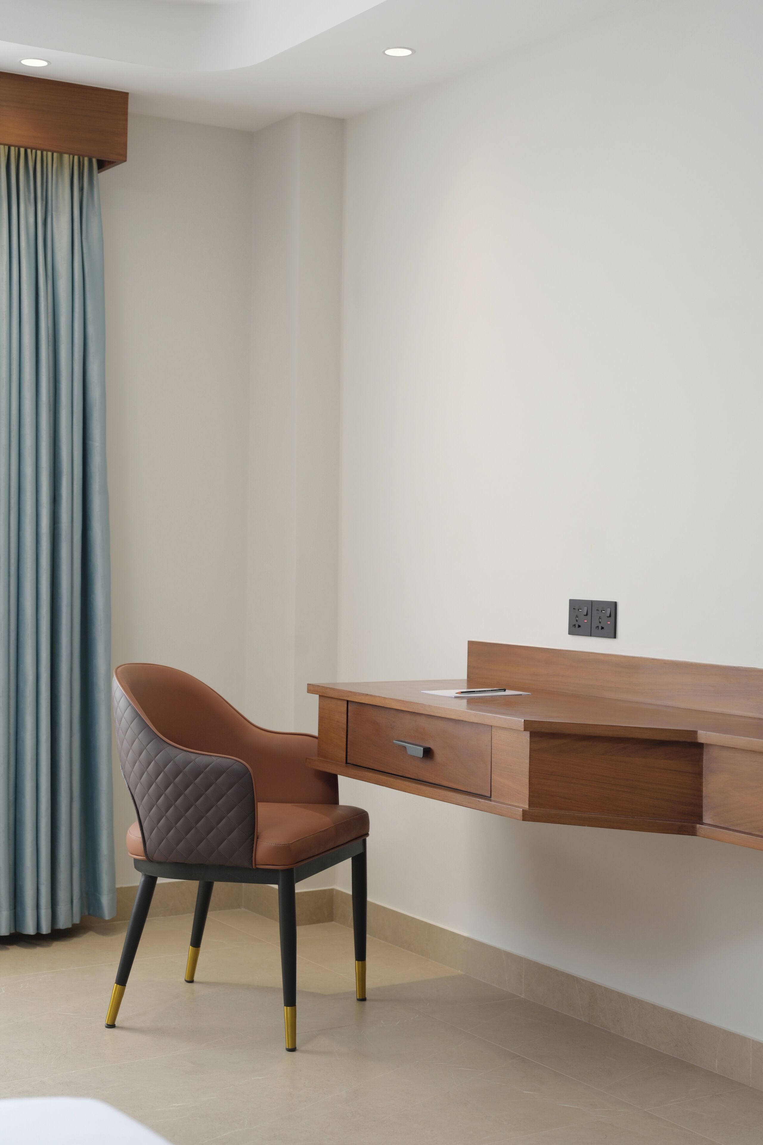 A modern office space with a wooden desk, a cushioned chair, and a power outlet on the wall.