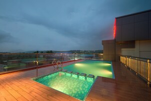Una piscina en la azotea con barandilla de cristal, terraza de madera y vistas a las montañas.