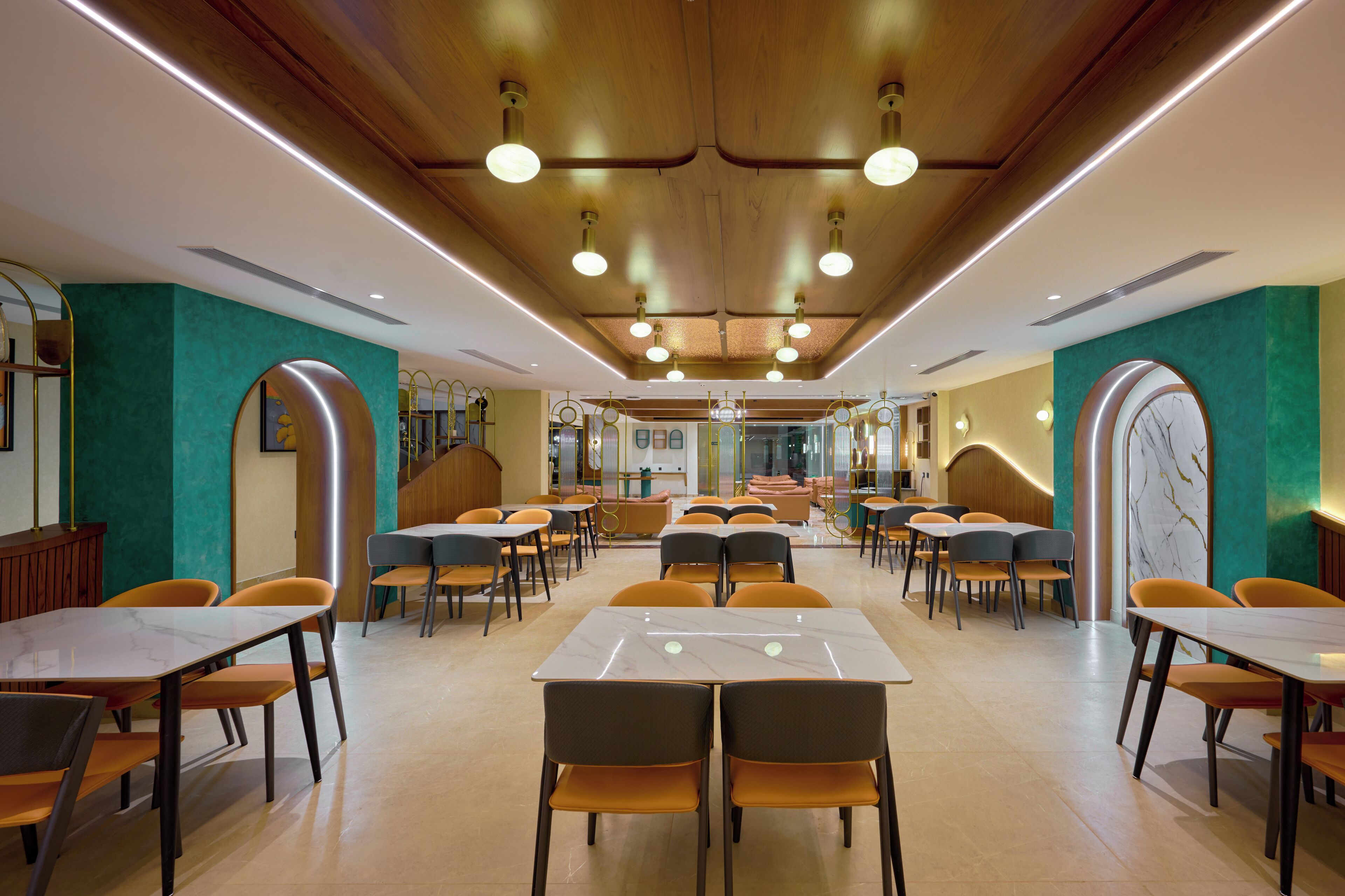 A spacious dining area with multiple tables and chairs, wooden ceiling with recessed lighting, and teal accent walls.