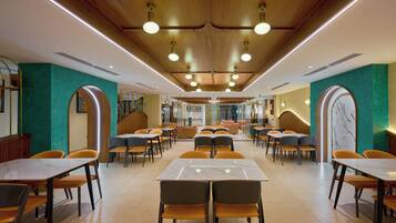 A spacious dining area with multiple tables and chairs, wooden ceiling with recessed lighting, and teal accent walls.