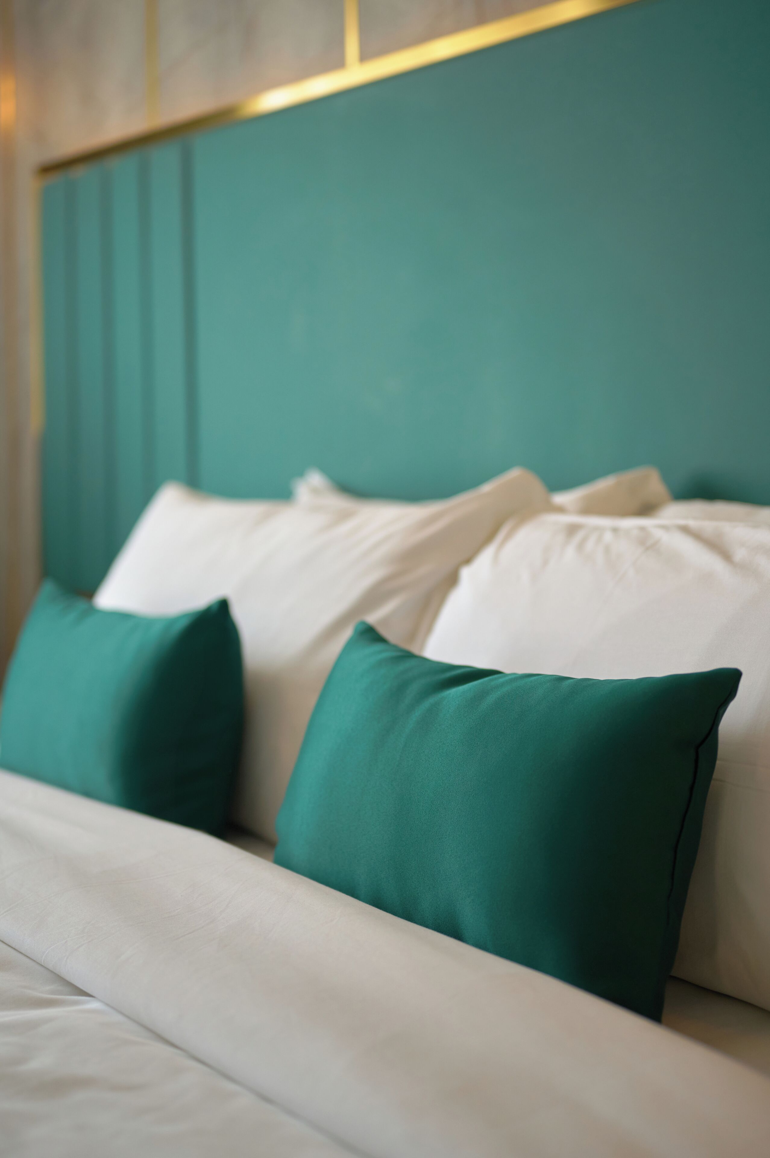 Una cama con ropa de cama verde azulado y blanca, un cabecero verde azulado y una almohada blanca.