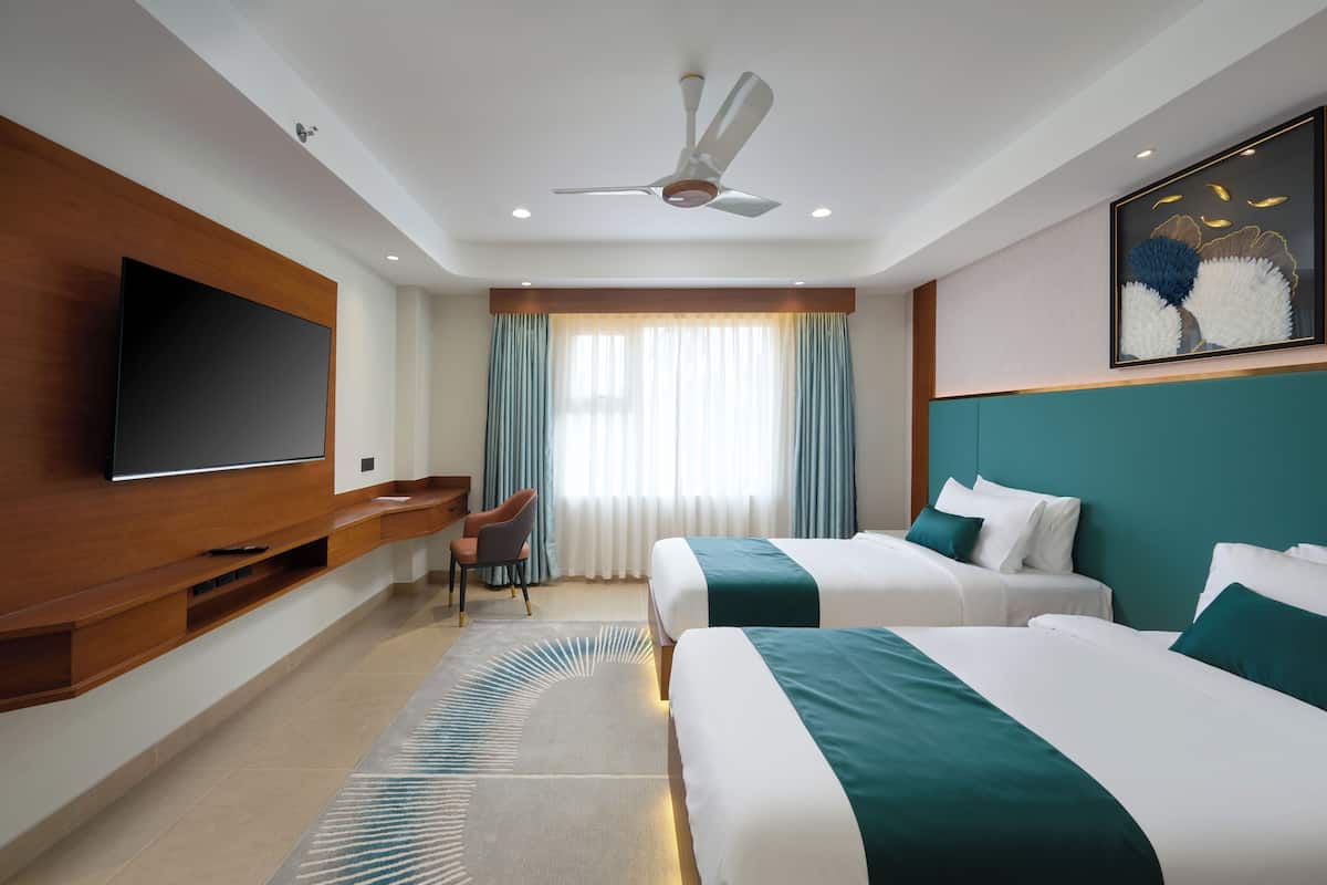 A hotel room with two beds, a flat-screen TV, a ceiling fan, and a large window with curtains.