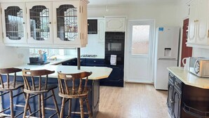 A kitchen with white cabinets, a central island with stools, a stove, oven, and a refrigerator. - Charming Luton Home for Families & Business Stays (Luton)