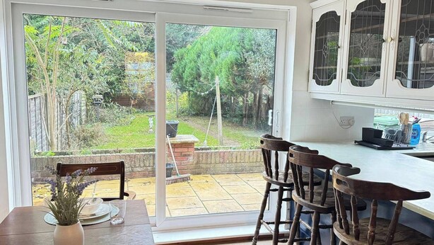 A kitchen with a sliding glass door leading to a garden. There is a dining table with chairs and a potted plant. - Charming Luton Home for Families & Business Stays (Luton)