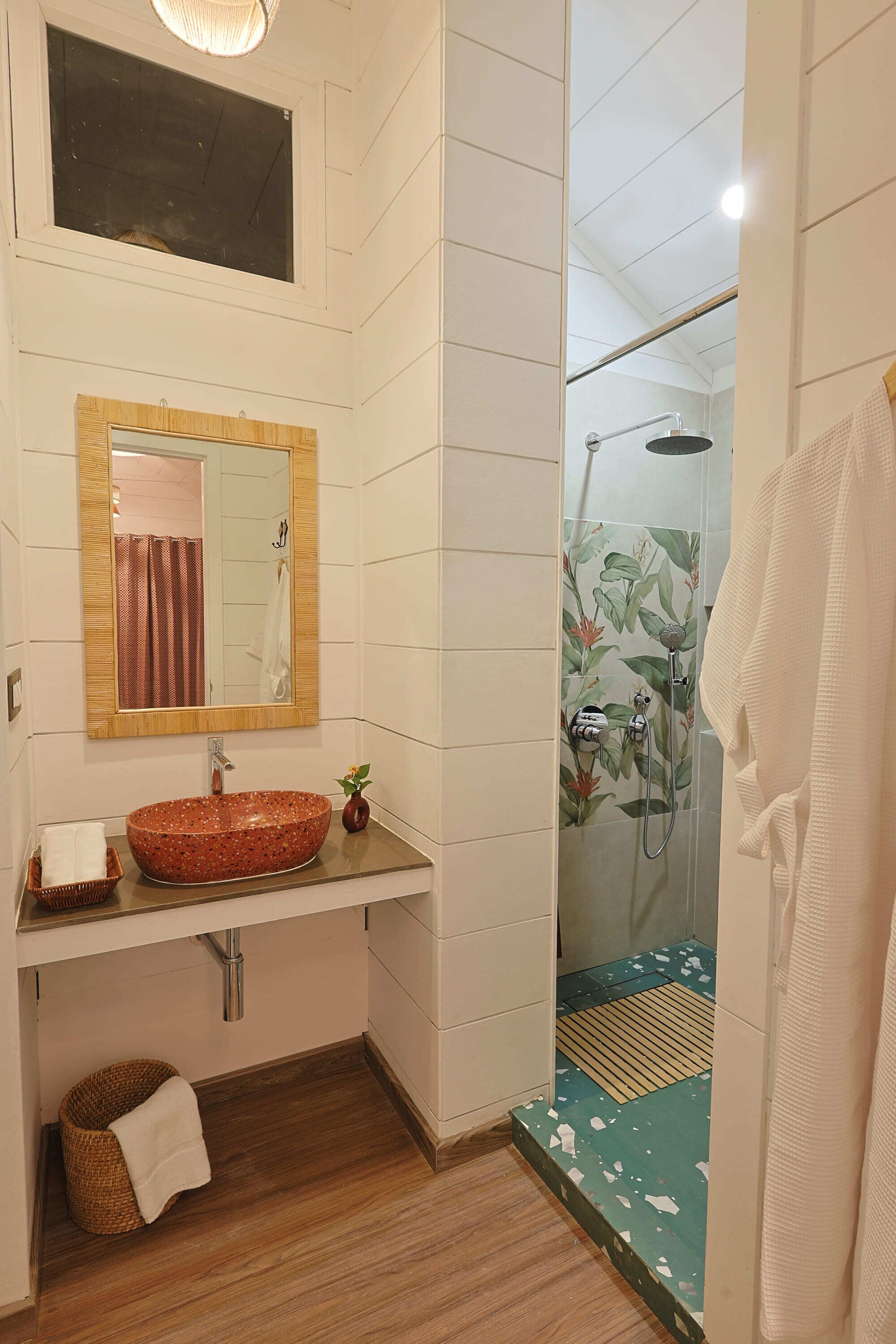 Un baño con tocador de madera, un espejo grande, un lavabo con un cuenco decorativo, una ducha con puerta de vidrio y un perchero para toallas.