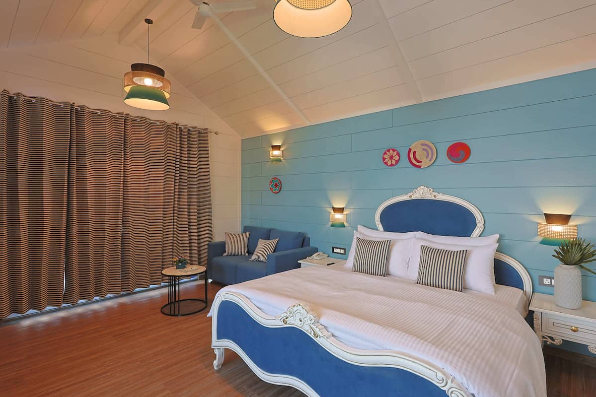 A bedroom with a blue headboard, a large bed, a blue sofa, and a small table.