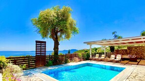 Una piscina con borde de piedra, cubierta de madera y un pérgola con asientos.