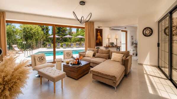 Un salon spacieux doté d’une grande fenêtre donnant sur une piscine, d’un ensemble de canapés et d’une table basse agrémentée d’objets décoratifs.