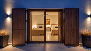 Habitación de hotel con puerta corrediza, una cama con cabecera, mesitas de noche y lámparas fijadas a la pared.