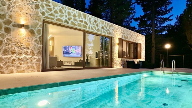 Une maison moderne avec une façade en pierre, une piscine et un téléviseur dans le salon.