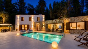 Un área de piscina moderna al aire libre con una pared de piedra, una piscina y asientos.