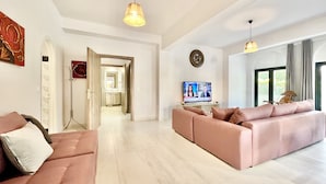 A spacious living area with a sofa set, a television, and a hallway leading to a bathroom.