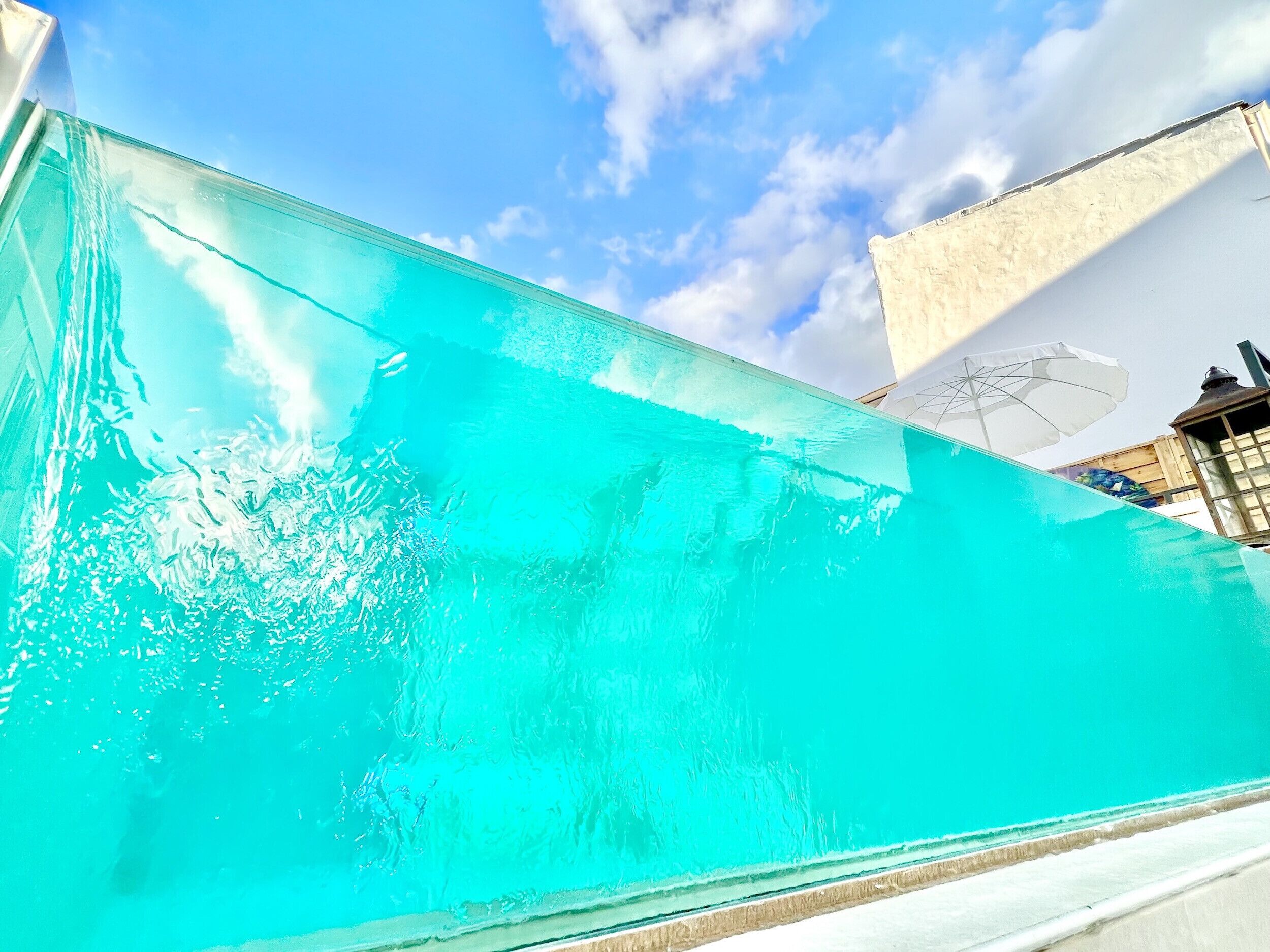 A clear view of a swimming pool with a white umbrella and a lantern nearby.