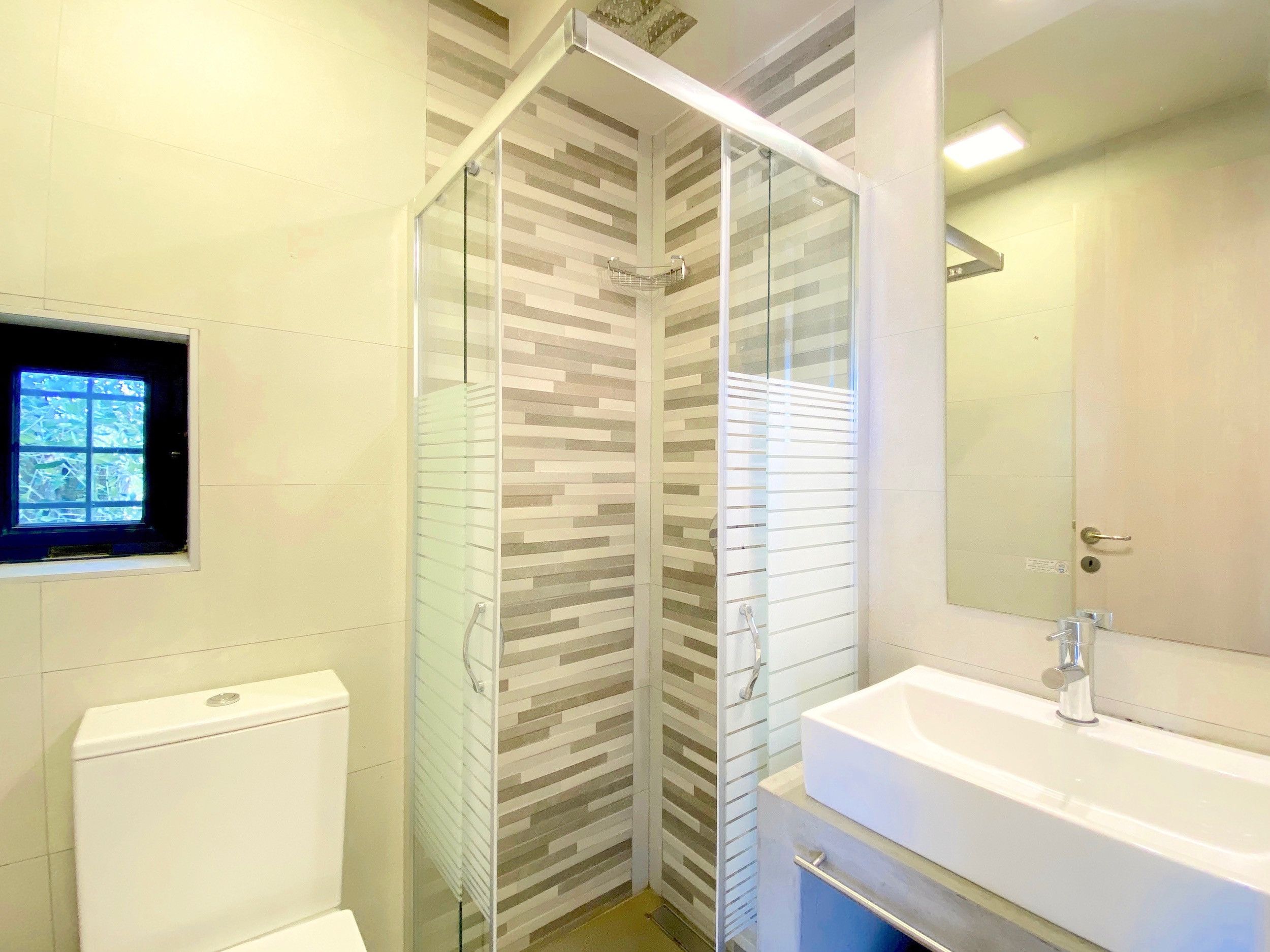 Ein modernes Badezimmer mit Duschkabine aus Glas, Toilette, Waschbecken und Spiegel.