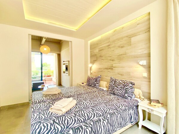 A bedroom with a bed, a bedside table, a wall-mounted light, and a view of the outdoors. - Barbati Beta MiniVilla with pool (Barbati)