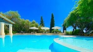 A clear blue swimming pool with steps leading into it, surrounded by lounge chairs and umbrellas.