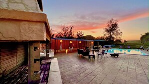 Ein Poolbereich mit Grillmöglichkeit, Sitzgelegenheiten im Freien und Blick auf den Sonnenuntergang.