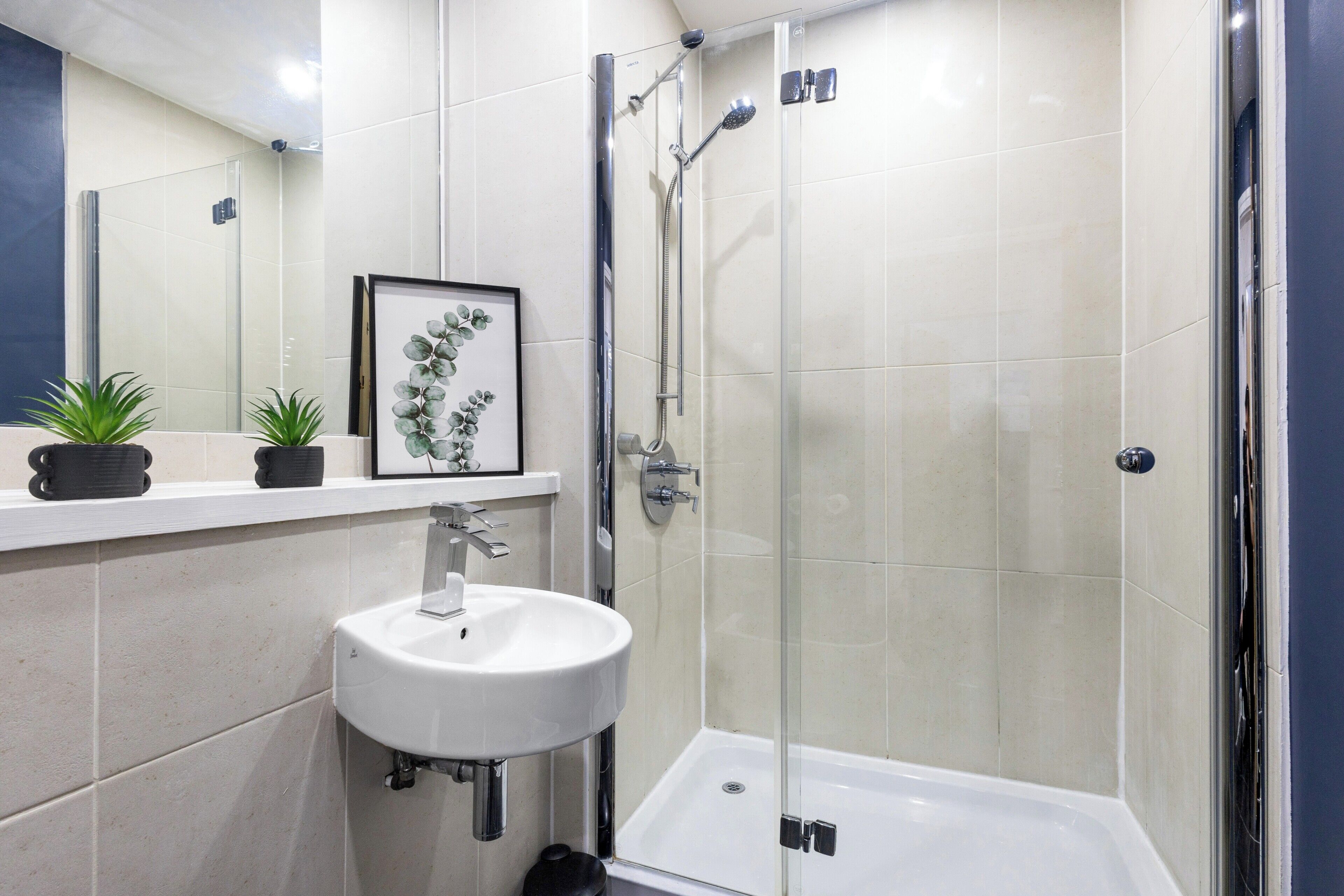 A modern bathroom with a glass-enclosed shower, a white sink, and a framed picture on the wall.