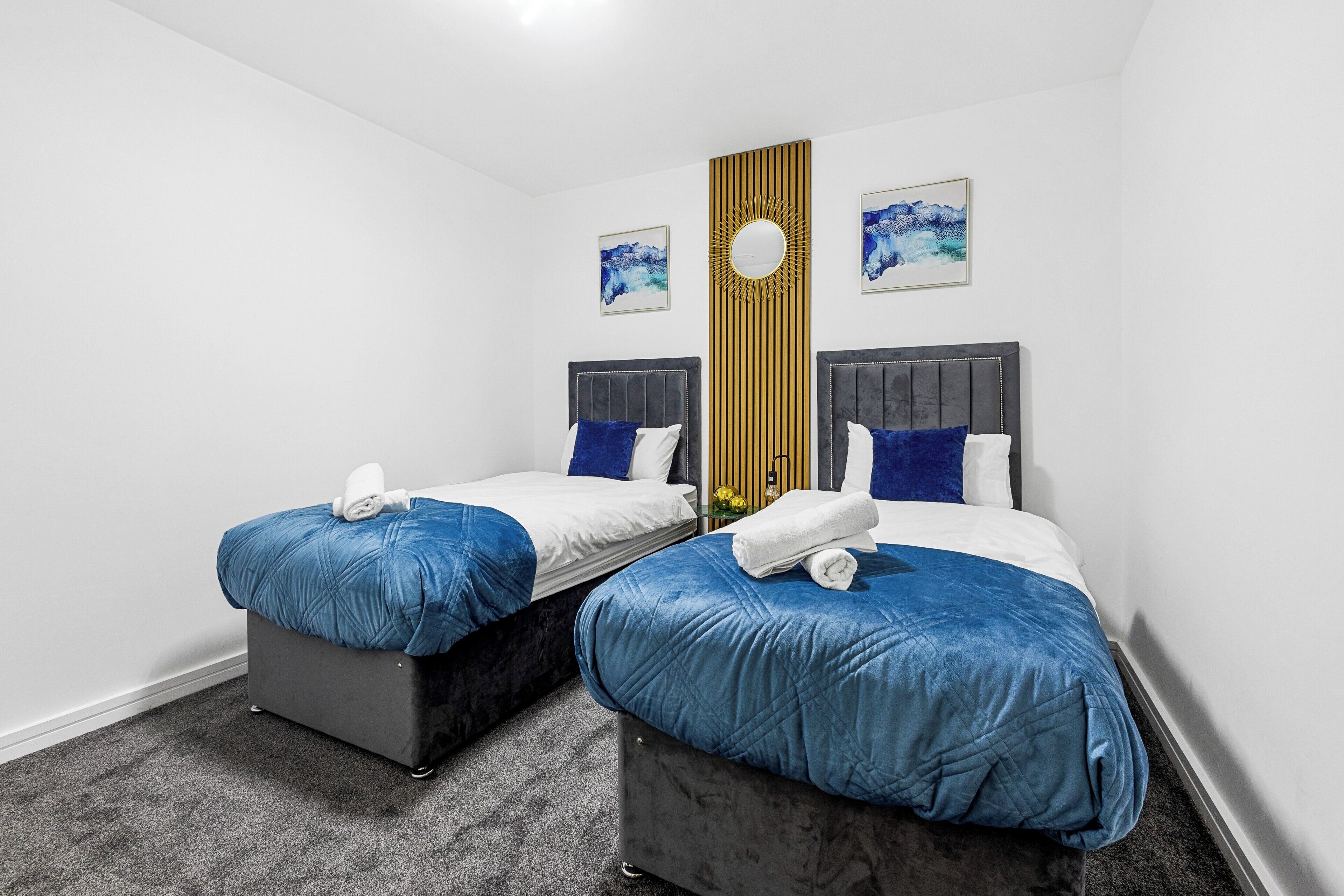 Ein Hotelzimmer mit zwei Betten, jeweils mit blauer gesteppter Bettdecke und weißen Kissen. An der Wand befindet sich eine dekorative Holzvertäfelung, darüber hängen zwei gerahmte Kunstwerke.