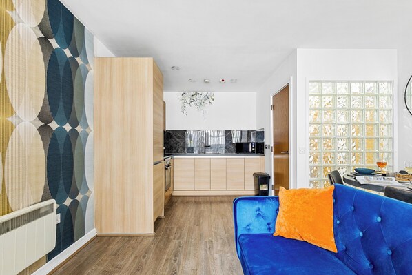 A modern kitchen with wooden cabinets, a black microwave, and a hanging light fixture. - Bullring Lux Suite- Netflix-free Parking-sleeps 6 (Birmingham)