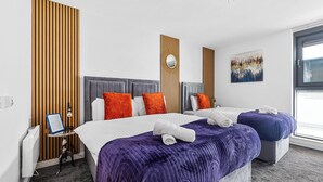 A hotel room with two beds, a large window, a wooden panel wall, and a painting. - Bullring Lux Suite- Netflix-free Parking-sleeps 6 (Birmingham)