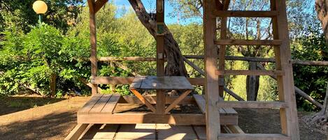Una mesa de picnic de madera bajo un refugio con el tronco de un árbol al fondo.