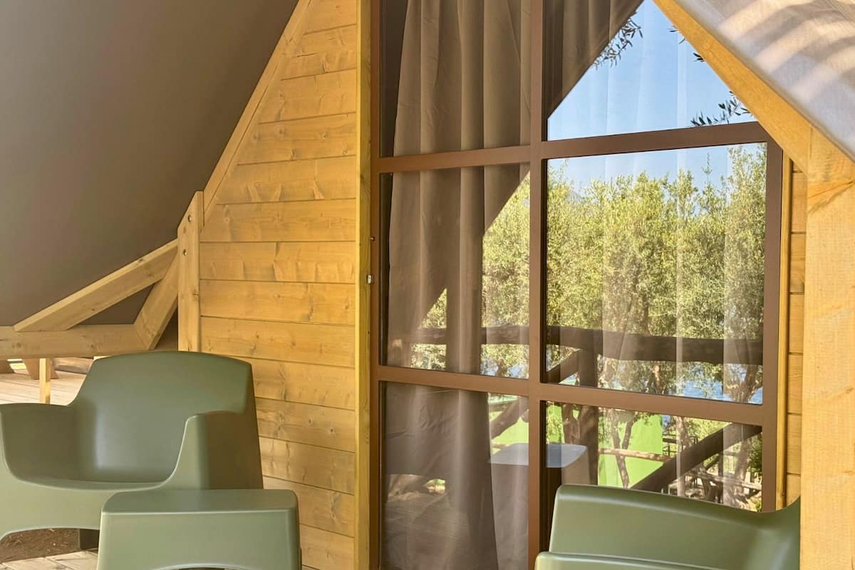 Une cabane en bois avec une grande fenêtre et deux chaises vertes.