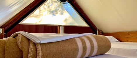 A cozy room with a bed, a fan, and a window with a view of trees.