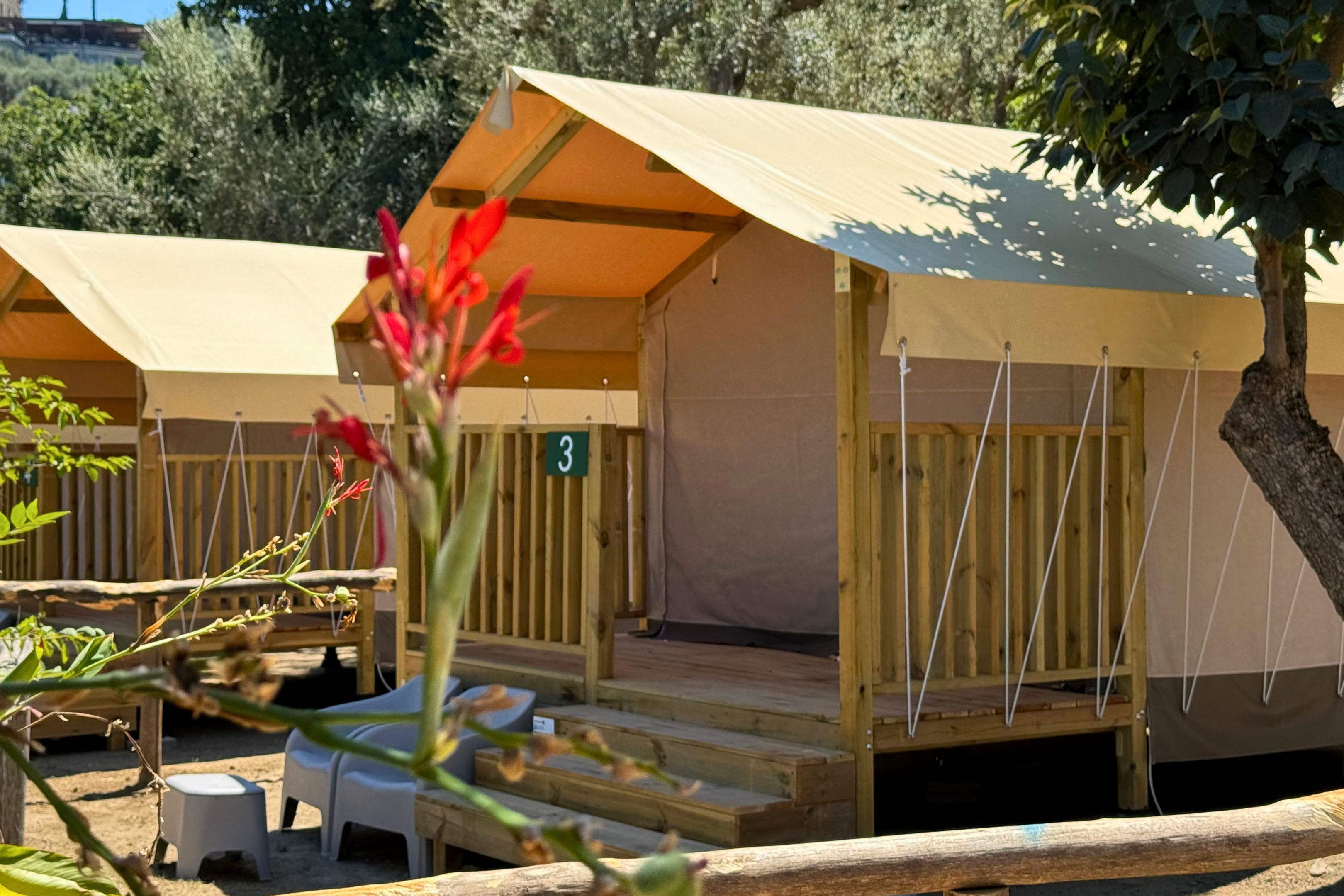A row of simple, tent-style accommodations with wooden railings and a number sign indicating room 3.
