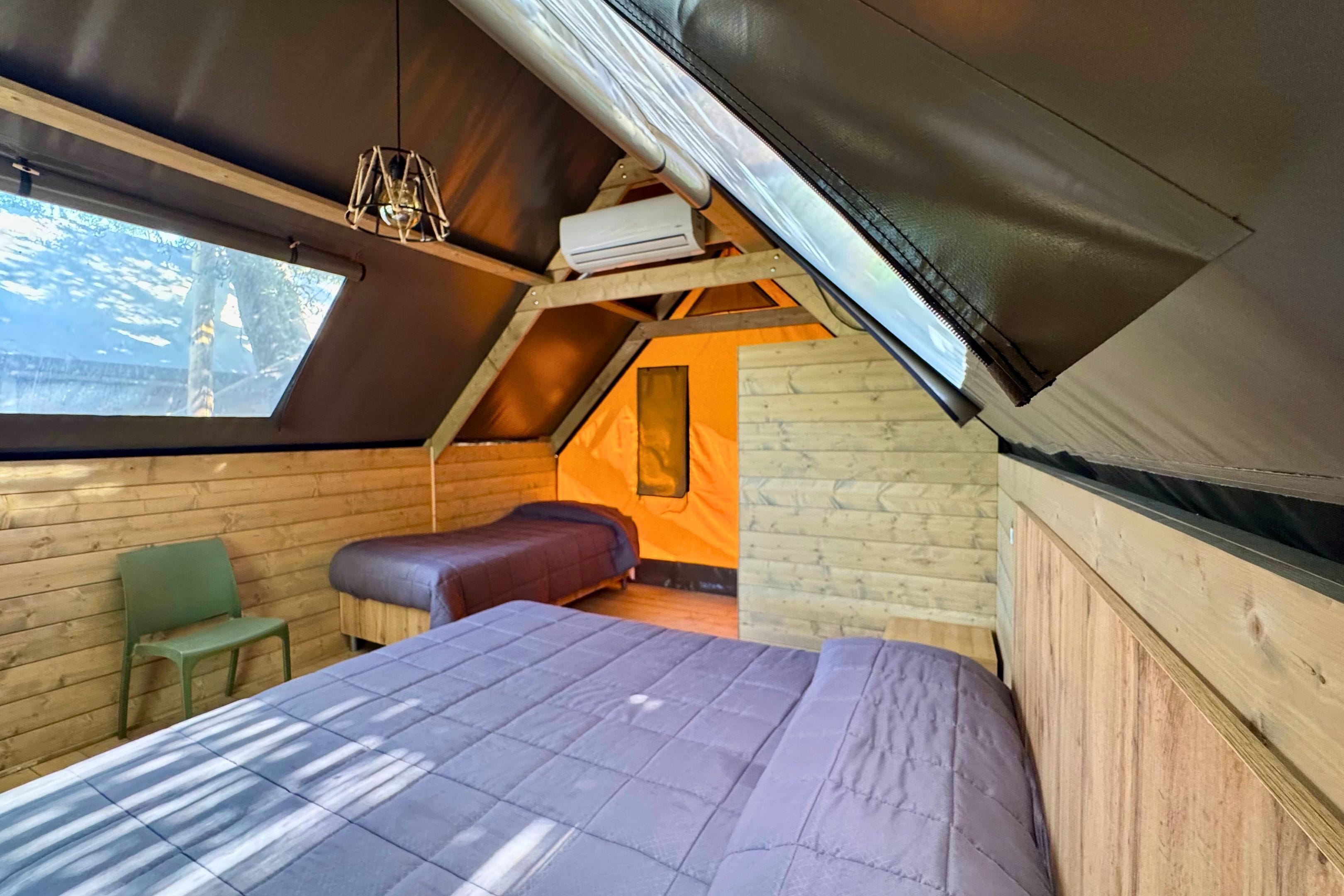 A cozy attic bedroom with a sloped ceiling, a large window, a bed, a chair, and a small table.
