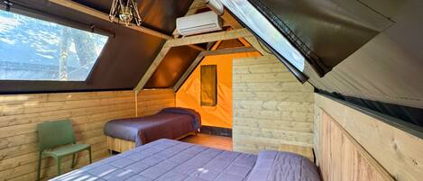 A cozy attic bedroom with a sloped ceiling, a large window, a bed, a chair, and a small table.