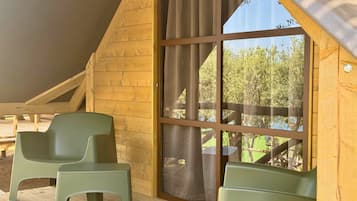 A wooden cabin with a large window, two green chairs, and a wooden deck.
