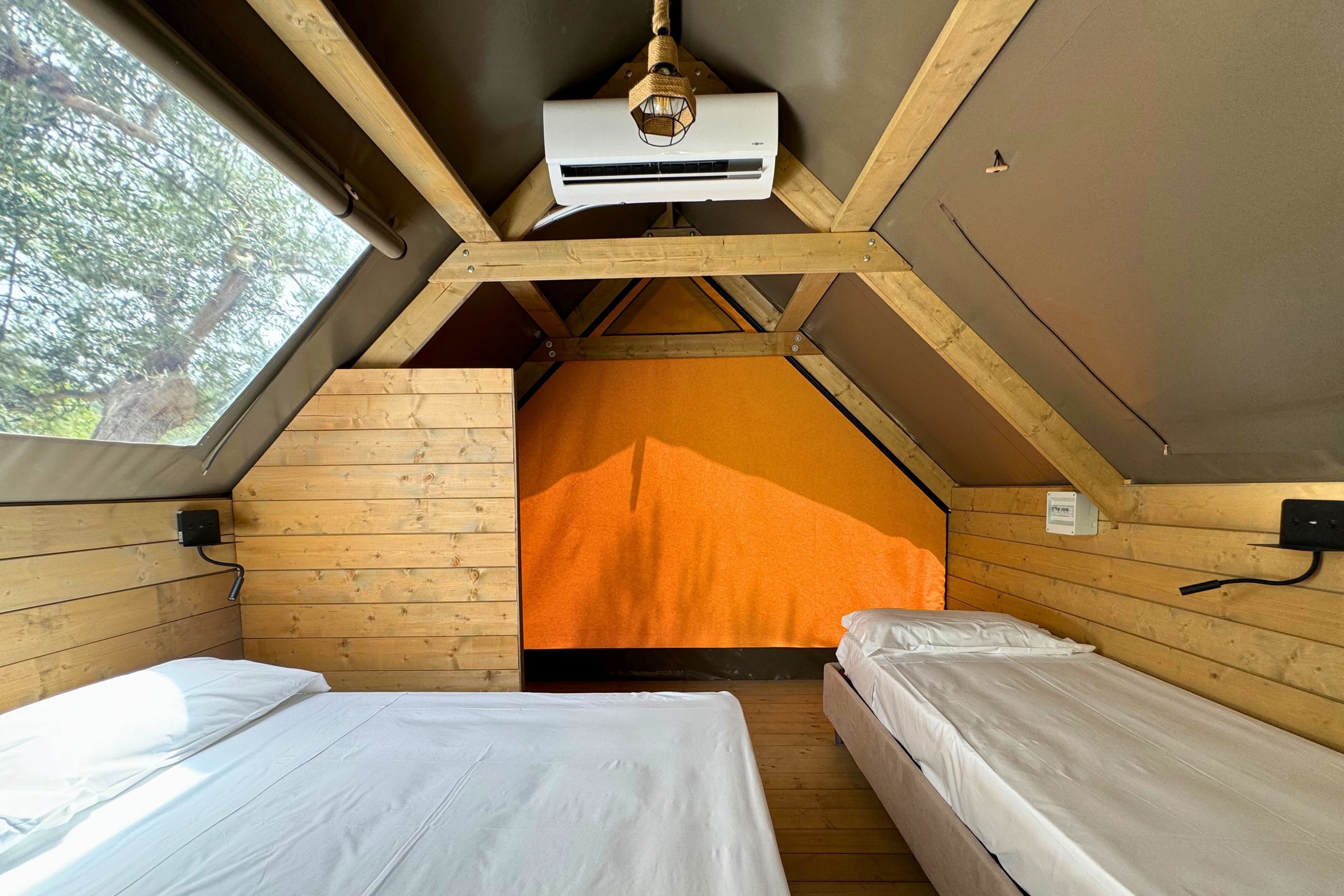 Una habitación pequeña y acogedora con dos camas, paredes de madera, techo inclinado y un ventanal grande.
