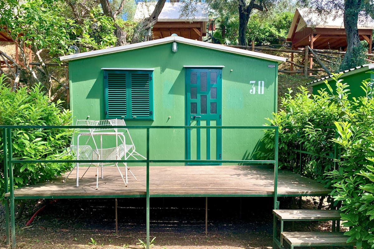 Un petit bâtiment vert, de plain-pied, doté d’une terrasse en bois, d’une chaise en métal et d’une petite table.