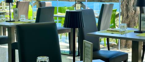 A restaurant with tables and chairs, a view of the sea, and a menu stand.