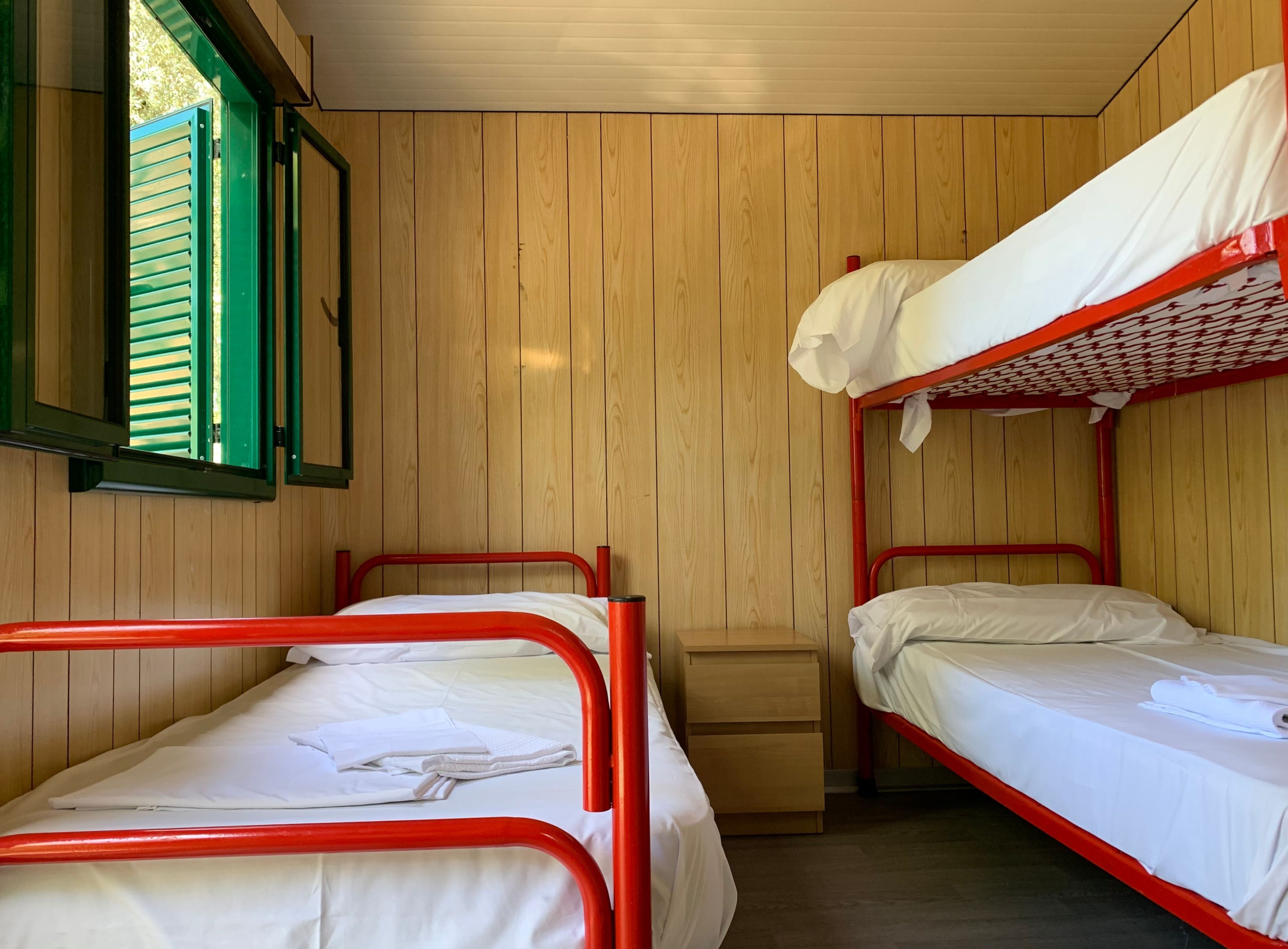 Une chambre de dortoir avec deux lits superposés, des murs en bois, une petite table de chevet en bois et une fenêtre avec des volets verts.