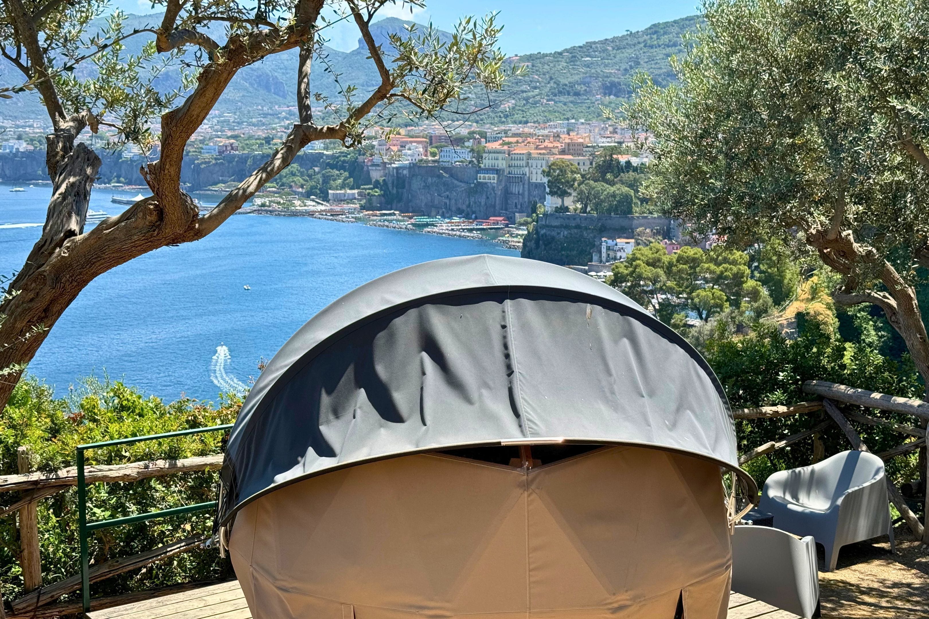 A tent set up on a wooden deck overlooking a coastal town with a clear view of the sea and buildings in the distance.