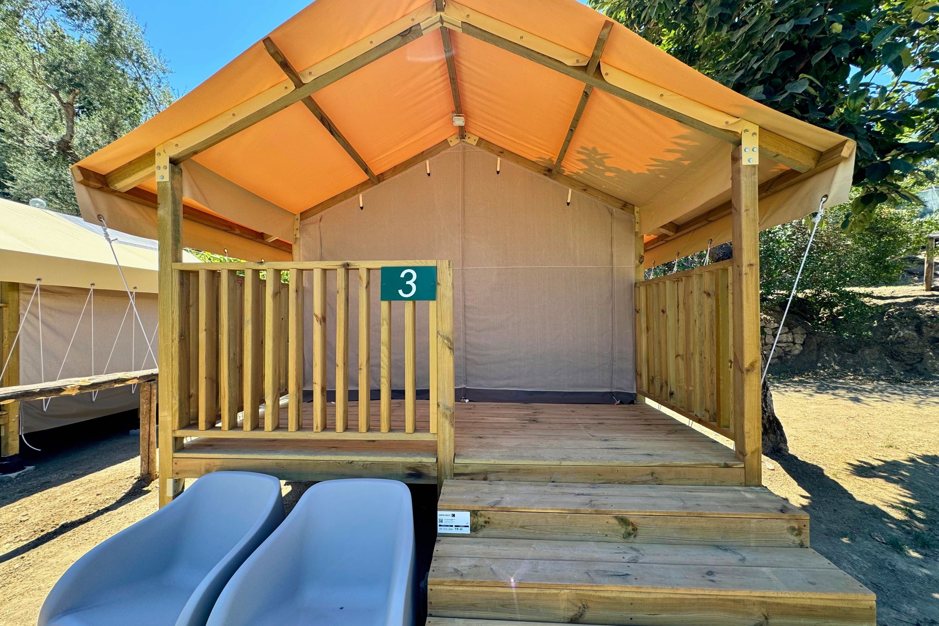 Een houten constructie met een bord met het nummer 3, een overdekte ingang en twee witte stoelen ervoor.