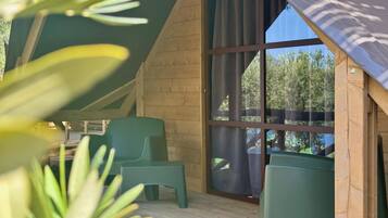 Una cabaña de madera con un ventanal grande, sillas verdes y una terraza de madera.