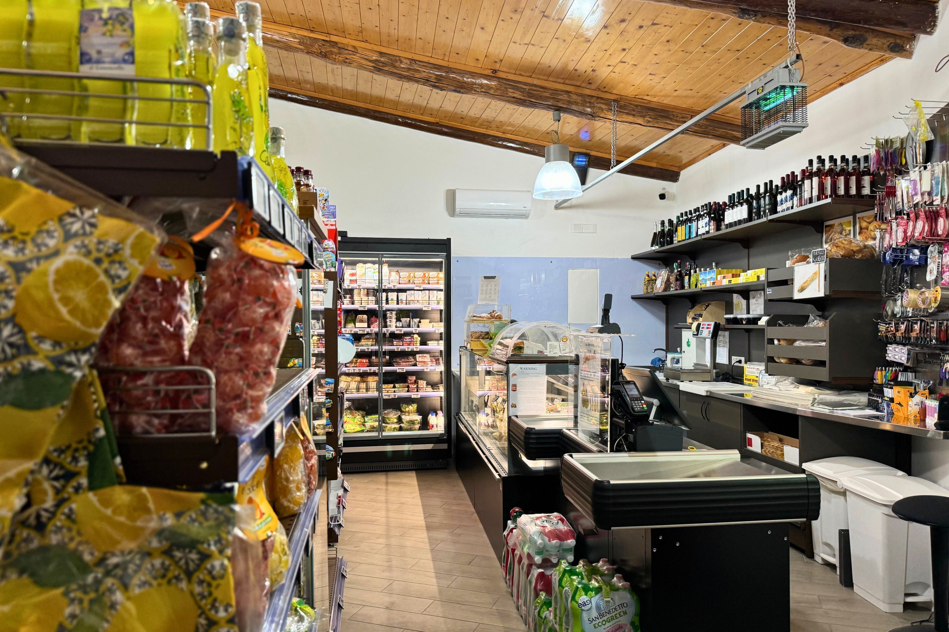 L’intérieur d’une épicerie, avec des étagères remplies de divers produits, un rayon réfrigéré et une zone de caisse.