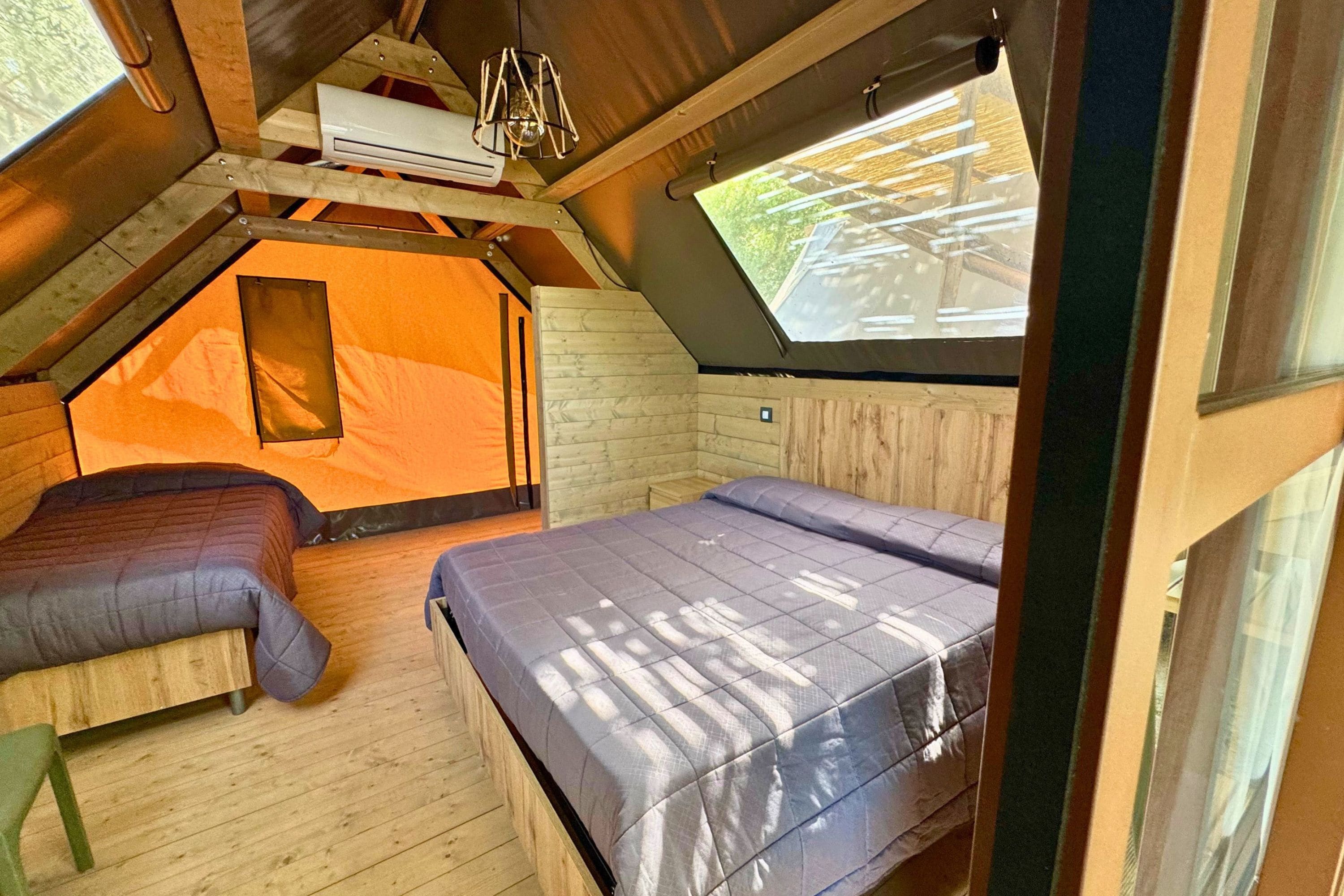 A cozy attic bedroom with a sloped ceiling, a wooden bunk bed, a small orange tent-like structure, and a skylight.